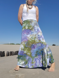 Person wearing a colorful floral skirt and white top on a beach.