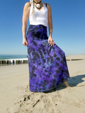 Person wearing a white top and purple patterned skirt on a beach.
