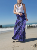 Woman wearing a white top and purple tie-dye skirt on a beach.