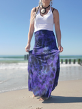 Woman wearing a white tank top and purple tie-dye skirt on a beach.