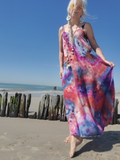 Woman in a colorful dress standing on a beach with clear blue sky.