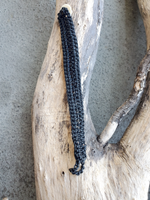 back side of the Black braided cord on a piece of driftwood against a concrete background