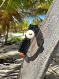 Black beaded bracelet with a white stone and orange bead on a wooden surface with palm leaves in the background