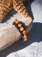 Bracelet with orange beads on a piece of driftwood next to a starfish on a sandy background