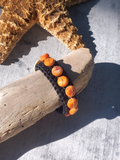 Bracelet with orange beads on a piece of driftwood next to a starfish on a sandy background