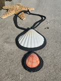 2 shells made into a statement necklace, laying on the sand
