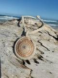 Necklace with a shell pendant on a piece of driftwood by the beach
