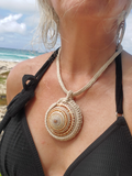 Person wearing a necklace with a large shell pendant on a beach
