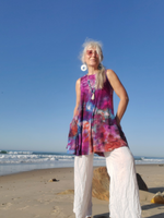 Woman standing on a beach wearing a colorful sleeveless top and white pants.
