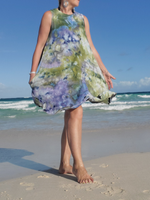 Woman in a floral dress standing on a beach with ocean waves in the background