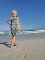Woman in a floral dress standing on a beach with clear blue sky and ocean.