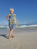 Woman in a floral dress standing on a beach with clear blue sky and ocean.