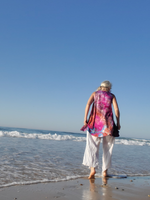 Person walking on a beach with a colorful top and white pants.