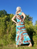 Woman wearing a tie-dye dress standing in a natural setting with trees and blue sky.