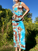 Woman wearing a tie-dye dress with blue and brown patterns standing in a natural setting.