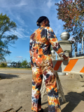 Person wearing a tie-dye outfit standing next to a roadblock with trees and blue sky in the background
