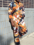 Person wearing a tie-dye outfit leaning against a tiled wall.