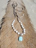 white pearls with a blue pendant, placed on a dry palm leaf at the beach