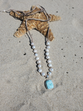 white pearls necklace with a light blue pendant layed on the sand and a starfish