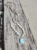 white beaded necklace with a blue pendant laying on an old piece of drift wood