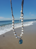the white beaded necklace is haning at the beach with the ocean in the back