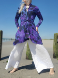 Person wearing a purple tie-dye top and white pants on a beach.