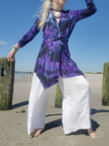 Person wearing a purple tie-dye top and white pants on a beach.