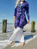 Person wearing a purple tie-dye dress and white pants on a beach.