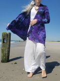 Person wearing a purple tie-dye shirt and white pants on a beach.