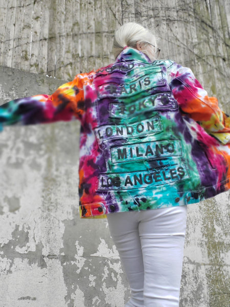 I'm modeling a Rainbow Galaxy Tie Dye WORLD TOUR jacket with the  words would tour Paris, Tokyo, London, Milan, Los Angels on the back. The words are printed on long square shaped denim patches with unfinished edges. These edges do frail, giving a more interesting and cool look to this style!