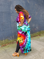 My best seller long short sleeve dress in bright rainbow tie dye. Mu is wearing a size 1XL; she's a curvy beauty.A side view of her, blaclk leggings showing at the side slit, hands on her hips. 