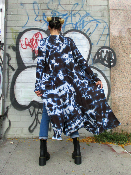 Back view of Mariana who's modeling this hand dyed black long duster. She is wearing a crop top, combat boots and skinny jeans with this piece. The wind is blowing the light weight cardigan a bit.