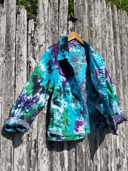Juniors Plus size denim jacket, cropped, with collar, chest pockets with metal buttons, button flaps, side and inner pockets. Photographed on the wooden fence, hanging on a hanger. Hand dyed in combo name NORTHERN LIGHTS - purple-green-jade-a bitof black. The mostly cotton fabric takes the dye beautifully!