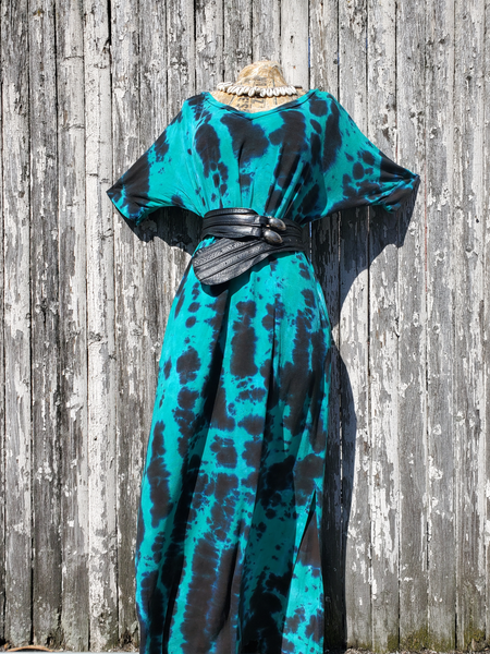 The same tie dye dress is displayed on a form, photographed front of our febce, held together with a wide black belt.